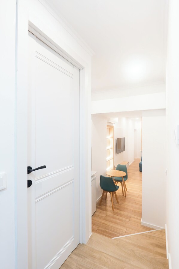 A hallway with a white door, wooden flooring, and a dining area with green chairs and a table.