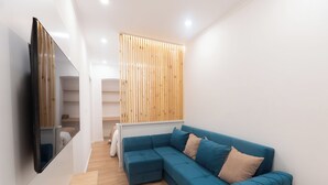 A modern living room with a blue sectional sofa, wooden slatted wall, and a flat-screen TV mounted on the wall.