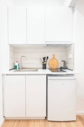 A compact kitchen with white cabinetry, a built-in sink, a small refrigerator, and a wooden cutting board.