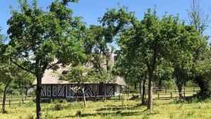 A traditional half-timbered house with a thatched roof, surrounded by a wooden fence and lush greenery.