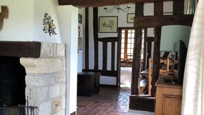 A traditional room with exposed wooden beams, a stone fireplace, and a view of the garden.