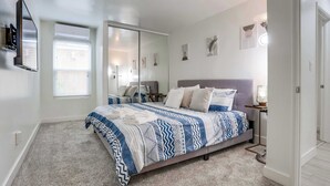 A bedroom with a bed, a TV mounted on the wall, a window with blinds, and a door. - Oceanview Condo 3 Blocks to La Jolla Beach (San Diego)