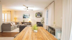 Un salon spacieux avec une table à manger en bois, un ensemble de canapés, une cheminée et un ventilateur de plafond.