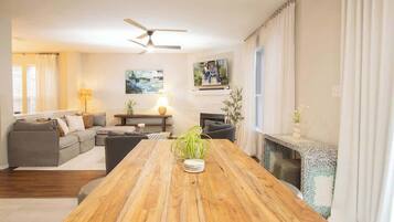 Amplia sala de estar con una mesa de comedor de madera, un conjunto de sofá, una chimenea y un ventilador de techo.