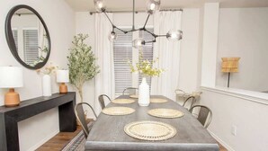 Un espace repas avec une longue table, des sets de table en fibres tressées et un lustre moderne.