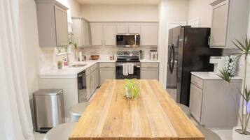 Una cocina moderna con una mesa de comedor de madera, electrodomésticos de acero inoxidable y armarios de colores claros.
