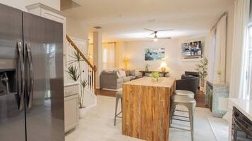 Una cocina moderna con una isla central, electrodomésticos de acero inoxidable y una escalera que sube a otro nivel.