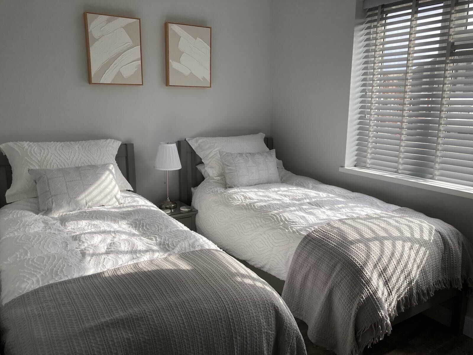 A bedroom with two beds, a nightstand, a lamp, and a window with blinds.