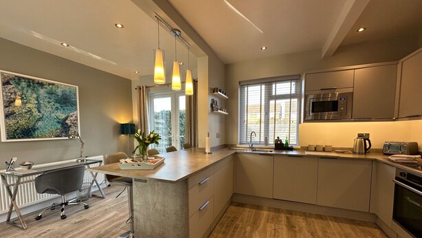 A modern kitchen with a central island, pendant lighting, and a view to the outdoors. - Stylish, Contemporary Home in Earl Shilton (Leicester)