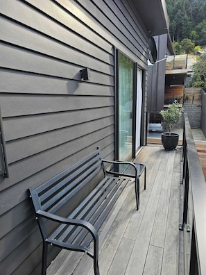 A wooden deck with a bench, a potted plant, and a sliding glass door leading to a balcony.