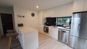 Una cocina moderna con una isla central, electrodomésticos de acero inoxidable y una ventana con vista a la vegetación.