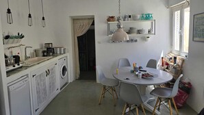 A compact kitchen with a washing machine, a dining table with chairs, and a hanging pendant light.