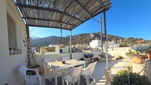 A rooftop terrace with a pergola, white furniture, and potted plants.