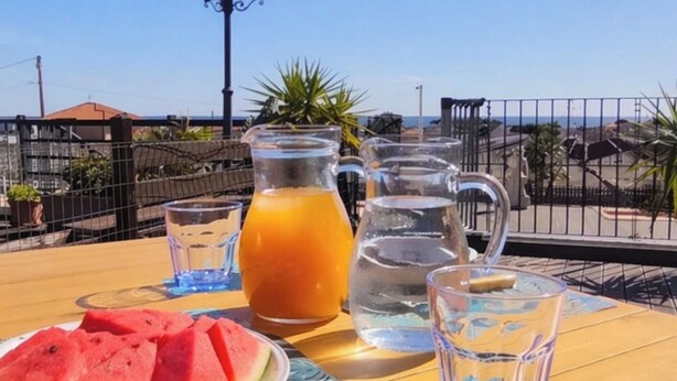 Una mesa con una jofaina de jugo de naranja, un vaso de agua, un vaso de té helado y un plato de rebanadas de sandía.
