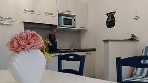 Una cocina moderna con armarios blancos, un microondas color turquesa y una mesa de comedor blanca con sillas.
