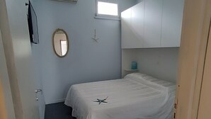 Un dormitorio con una cama, un ventanal pequeño, una decoración de estrella de mar y un ventilador de techo.