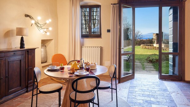 A dining area with a round table, four chairs, a lamp, a vase, and a window with curtains.