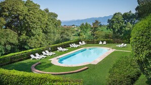 A swimming pool surrounded by neatly trimmed hedges and white lounge chairs.
