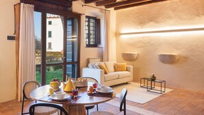 A cozy dining area with a round table set for breakfast, a sofa with cushions, and a view of the outside.