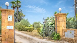 Une entrée fermée par un portail, agrémentée d’un panneau indiquant la présence d’un système de surveillance et d’un autre panneau indiquant « Jardin Chic ».