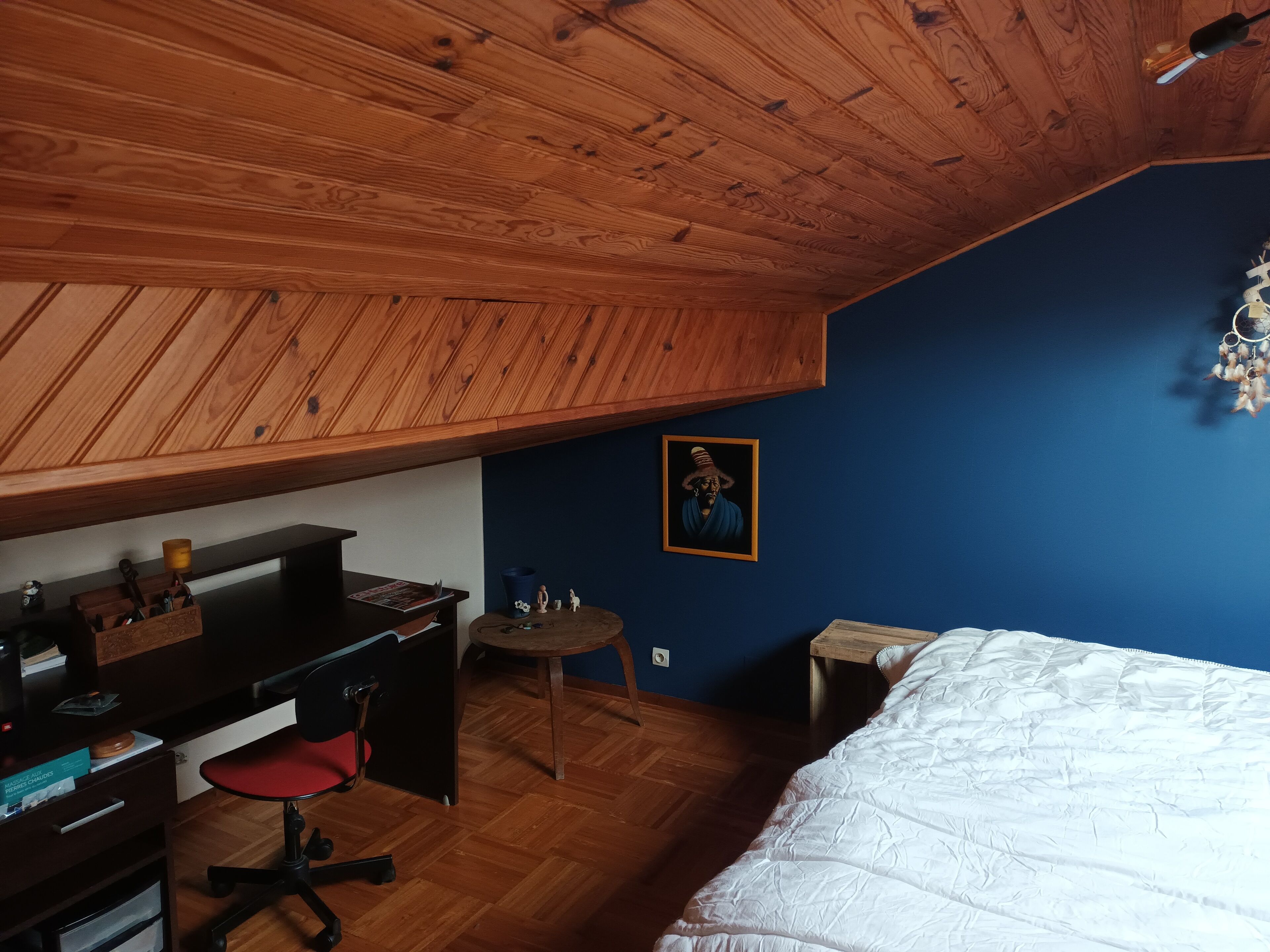 Un dormitorio con techo inclinado, escritorio de madera, silla y cama con edredón blanco.
