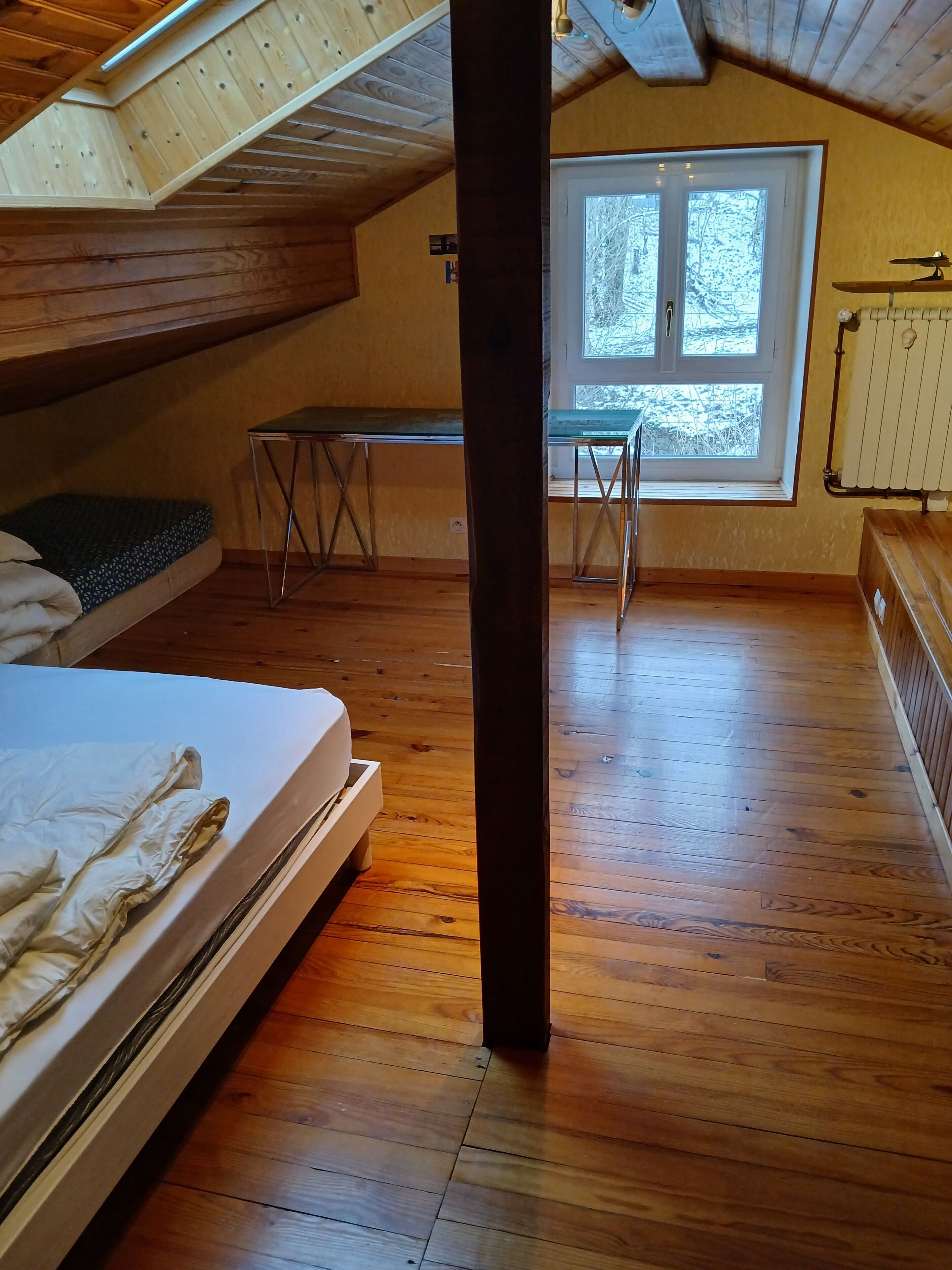 Une pièce avec un plafond en pente, un lit, une table et une fenêtre.
