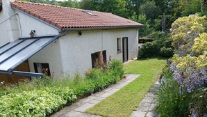 Una casa con tejado de tejas rojas, un pequeño jardín con un sendero empedrado y una variedad de plantas y flores.