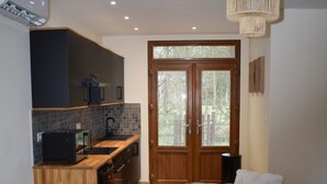 A modern kitchen with dark cabinetry, a wooden countertop, and a built-in oven. There is a dining area with two sofas and a rug. A large wooden door with glass panels is visible in the background. - Bungalow 15 in Villereal Rives Southwest France (Rives)