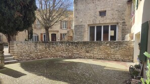 A courtyard with a stone wall, a tree, and a building with multiple windows and doors. - Detached 50 m2 apartment in village house. (CAROMB)
