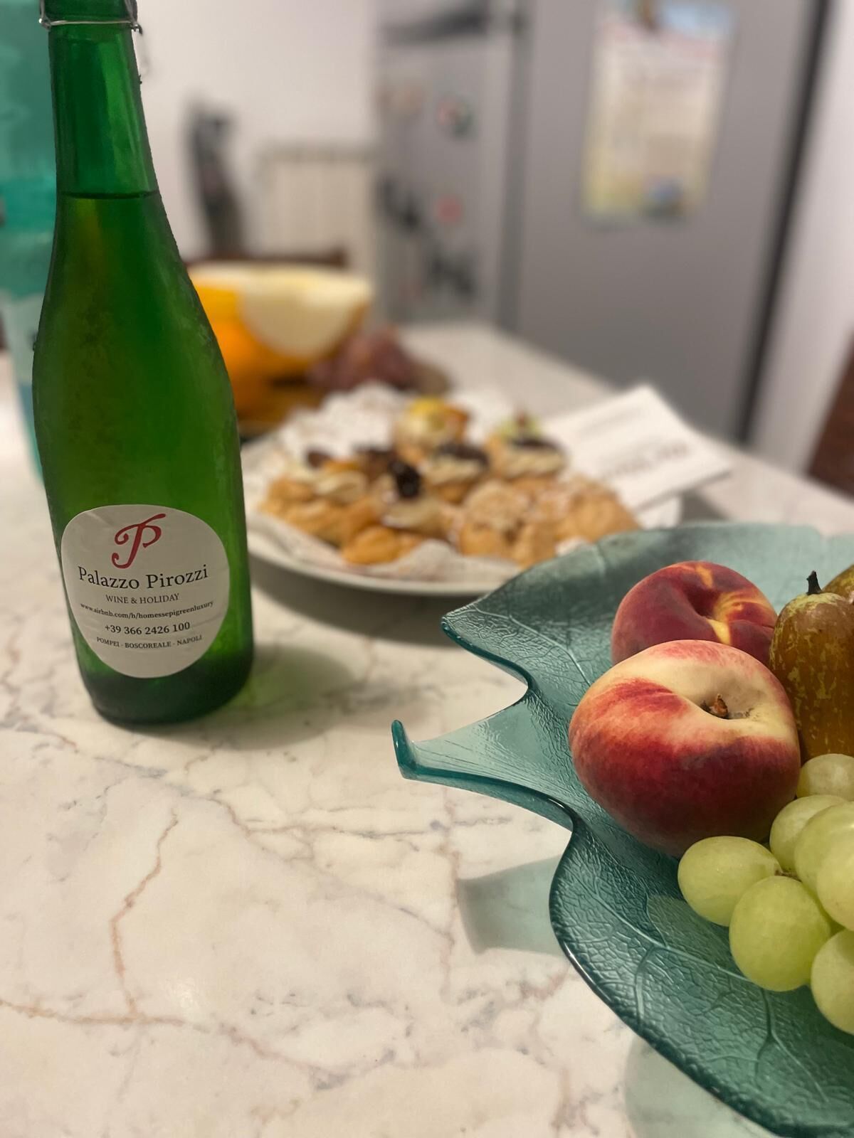 A green bottle labeled "Palazzo Pirozzl" on a marble countertop with a plate of food and fruits.
