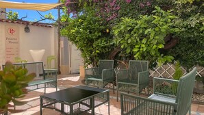 Ein Terrassenbereich im Freien mit grünen Metallstühlen und einem schwarzen Tisch, umgeben von üppiger Bepflanzung und blühenden Pflanzen.