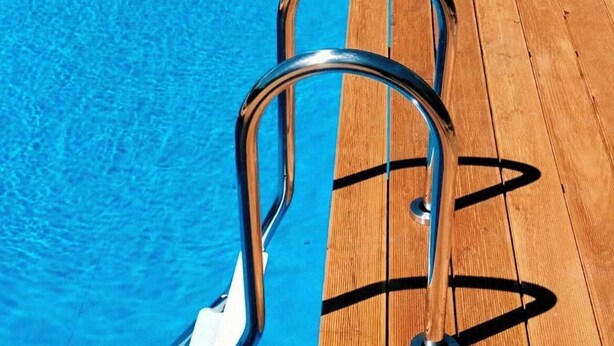 Eine Holzterrasse mit einer Metallleiter, die zu einem Pool führt.