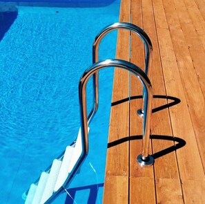 Een houten terras met een metalen zwemplatform naar het zwembad.