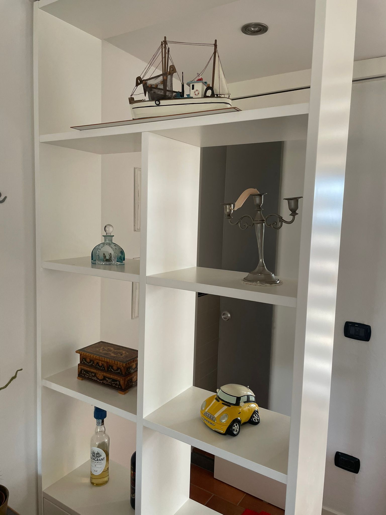 A white shelving unit with various items including a model ship, a bottle, a toy car, and a decorative lamp.