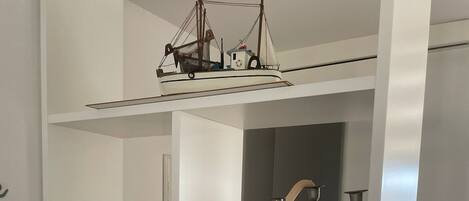 A white shelving unit with various items including a model ship, a bottle, a toy car, and a decorative lamp.