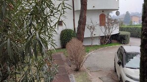 Ein Wohngebäude mit einem bogenförmigen Balkon, einem Baum im Vordergrund und einem parkenden Auto.