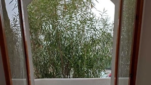 Ein offener Balkon mit zwei weißen Sitzgelegenheiten und einem kleinen runden Tisch, umgeben von einem Betonboden und Blick auf dichtes Grün.