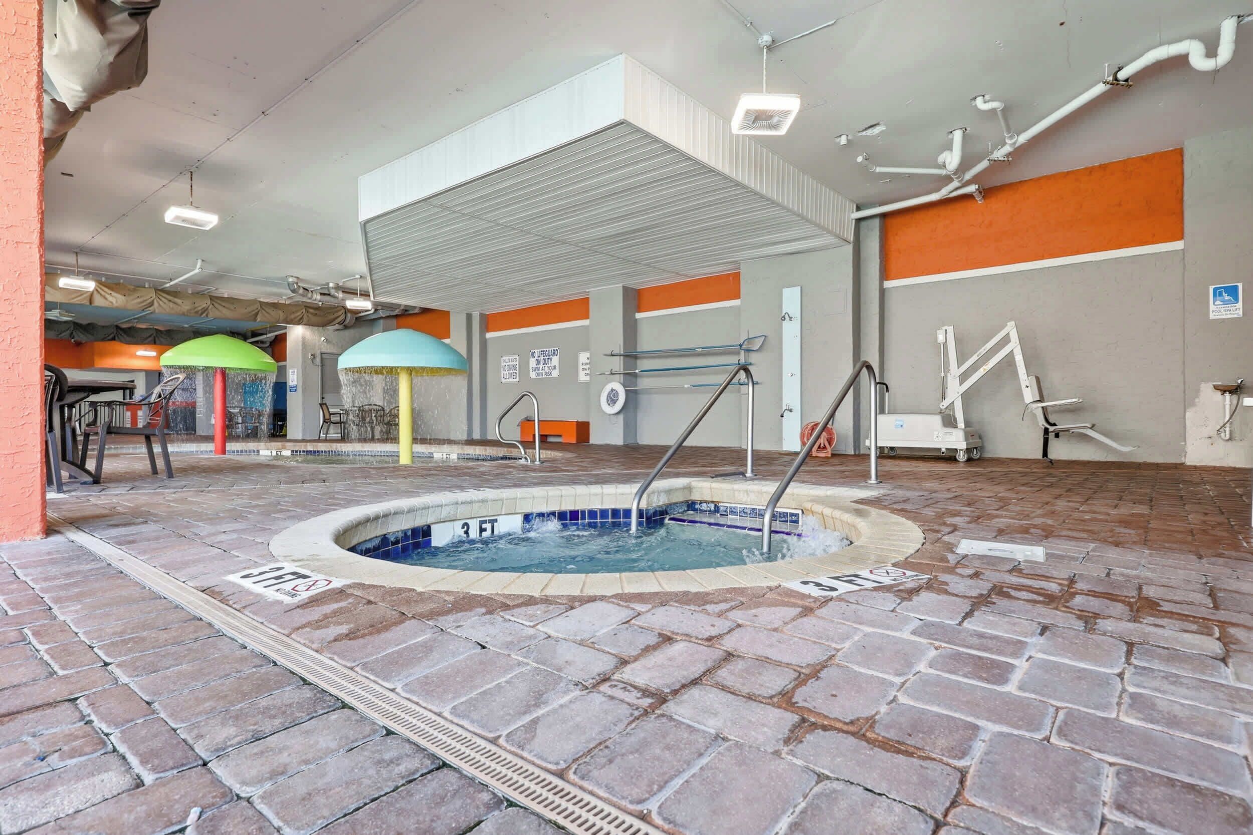 An indoor swimming pool with a brick floor, a diving board, and a lifeguard stand.