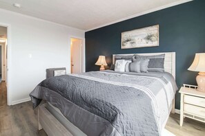Une chambre à coucher avec un lit, des lampes de chevet, un tableau au mur et une porte donnant sur une autre pièce.