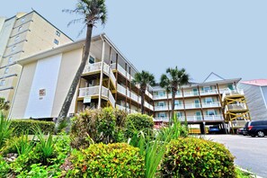 Un hôtel à plusieurs étages doté de balcons, d’un parking et d’une végétation luxuriante.