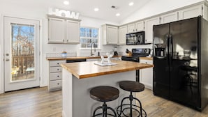 Una cocina moderna con armarios blancos, un refrigerador negro e isla de madera con taburetes.