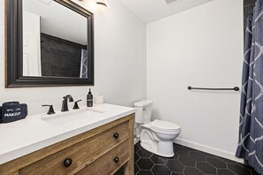 Un baño con tocador blanco, espejo, inodoro y cortina de ducha.