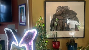 A living room with a large framed artwork, a flat-screen TV, and various potted plants.
