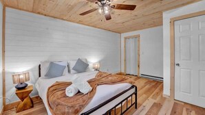 A bedroom with a wooden ceiling, a bed with white bedding, a brown blanket, and a ceiling fan. - Charming Pocono Boutique | Firepits | Pickleball (Monroe County)
