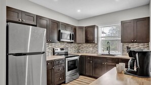 A modern kitchen with dark wood cabinets, stainless steel appliances, and a tiled backsplash.