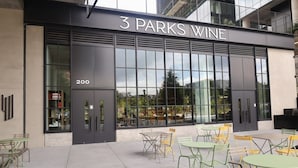 The exterior of 3 Parks Wine, featuring large glass windows, outdoor seating with green and yellow chairs, and a modern architectural design. - Jade Junction (Atlanta)