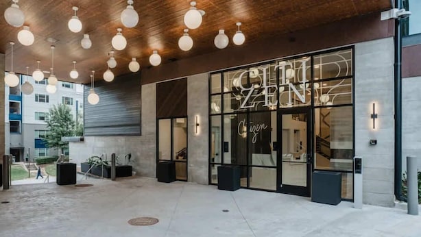 A modern building entrance with a glass facade, a visible staircase, and hanging spherical lights. - Jade Junction (Atlanta)