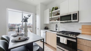 A modern kitchen with white cabinets, a stainless steel stove, and a microwave. - Jade Junction (Atlanta)