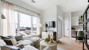 A modern living room with a sofa, coffee table, and a TV. There is a kitchen area visible in the background. - Jade Junction (Atlanta)