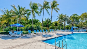 Ein Swimmingpool mit blauen Liegestühlen und Sonnenschirmen, umgeben von Palmen.